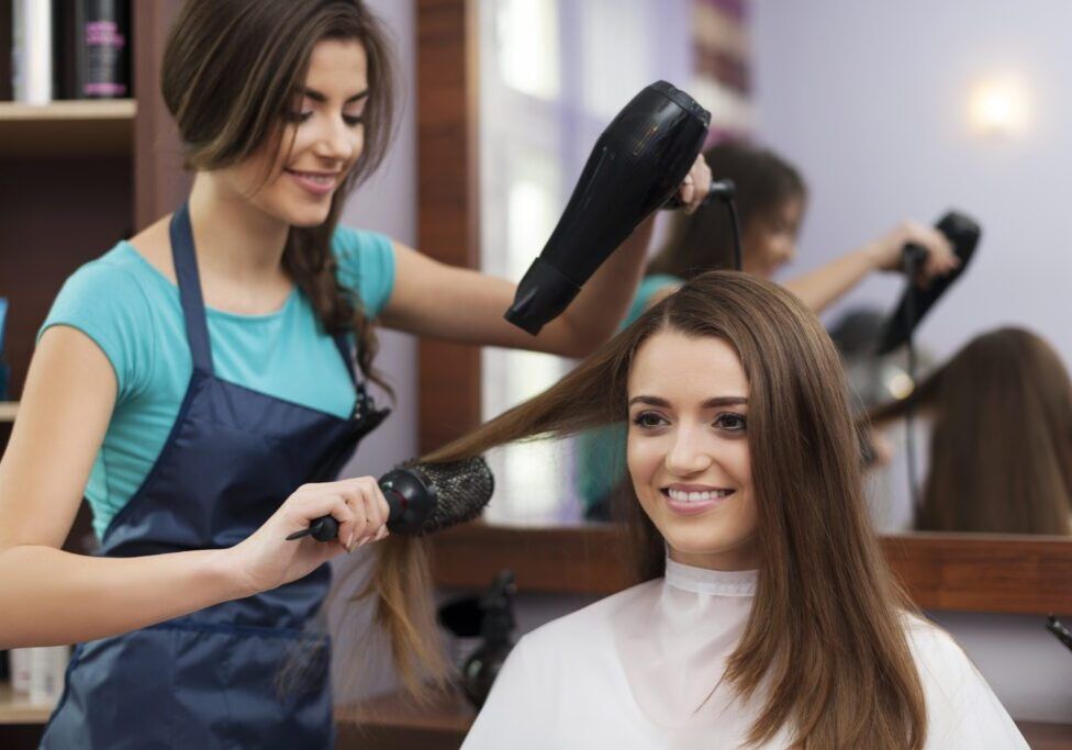 Female hairdresser using hairbrush and hair dryer